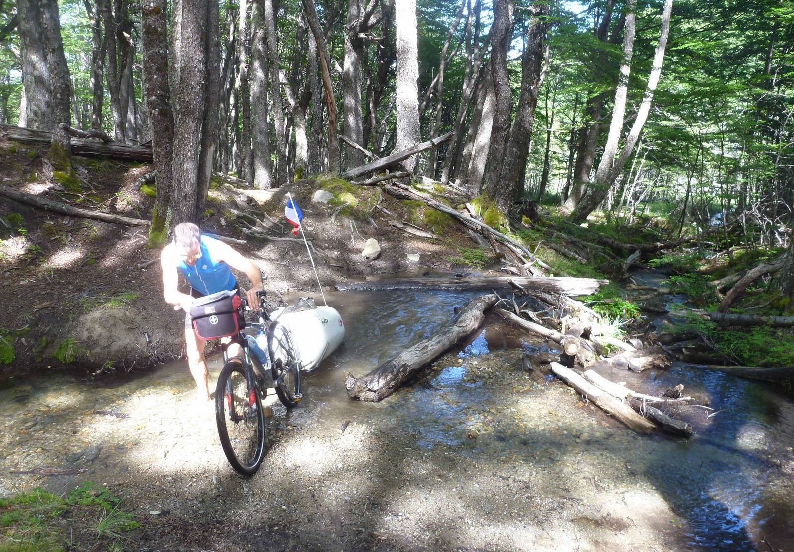 Voyageurs poussant un vélo et sa remorque sur un passage en bois au-dessus d’un ruisseau