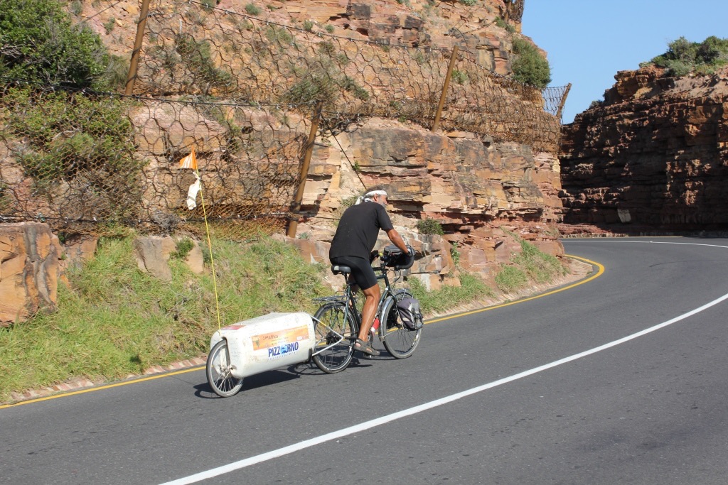 Cycliste et remorque dans un virage bordé de falaises