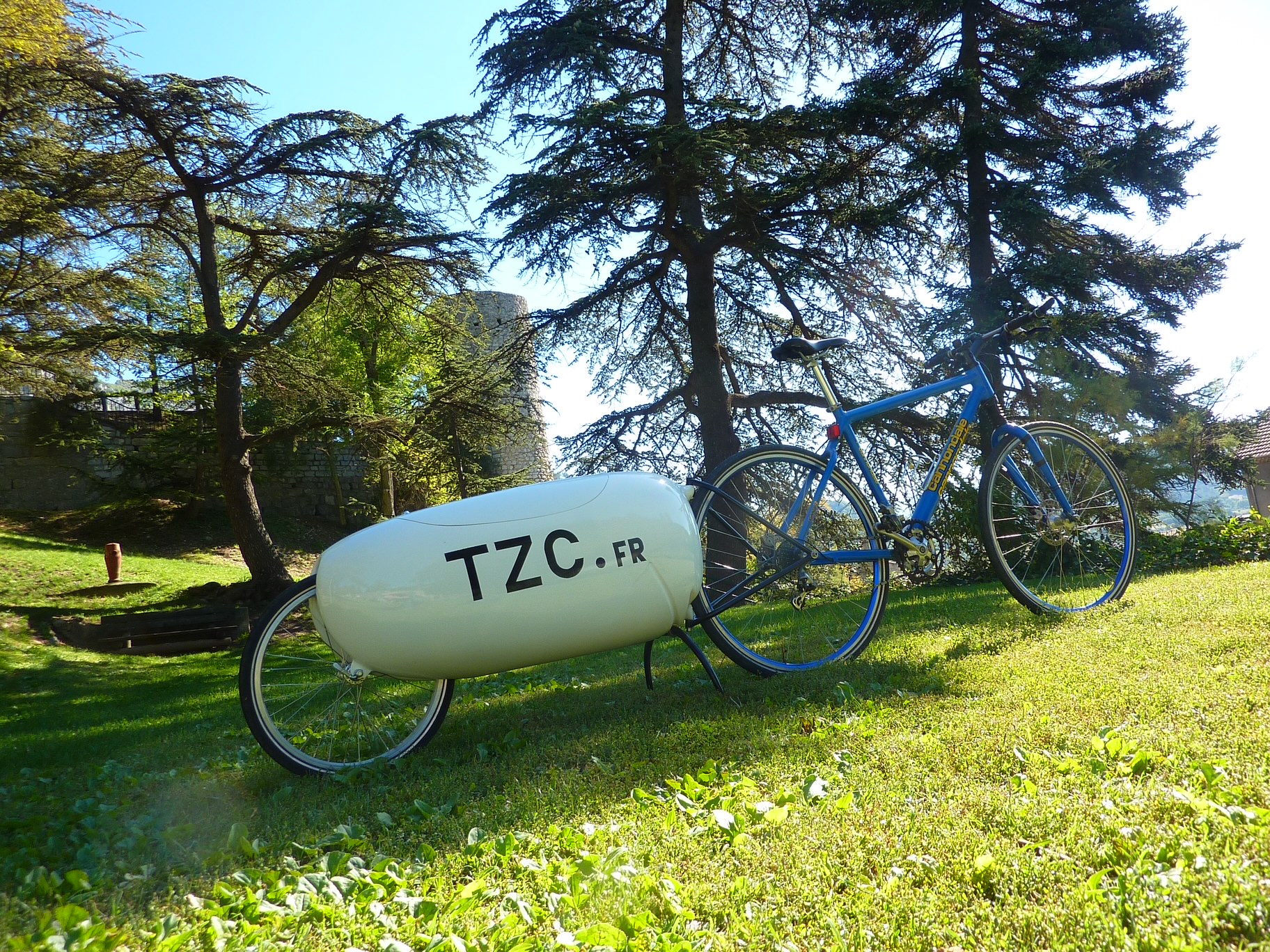 Remorque blanche TZC attelée à un vélo bleu dans un jardin